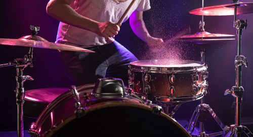 The drummer plays the drums. Beautiful blue and red background, with rays of light. Beautiful special effects smoke and lighting. The process of playing a musical instrument. The concept of music. Close-up photo.